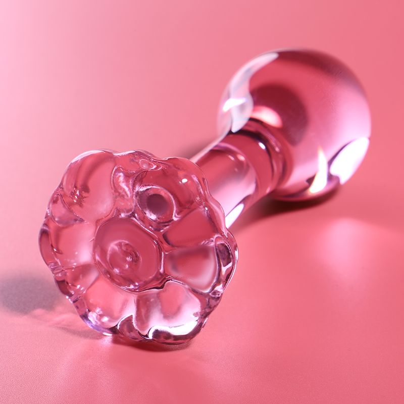 Plug anal en verre rose avec base détaillée en forme de fleur sur fond rose.