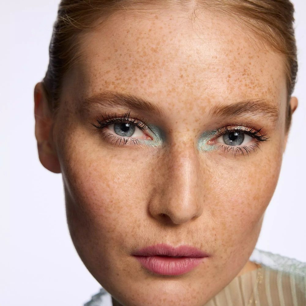 Gros plan d'un visage maquillé. Fard à paupières bleu clair. Taches de rousseur, yeux bleus, lèvres roses.