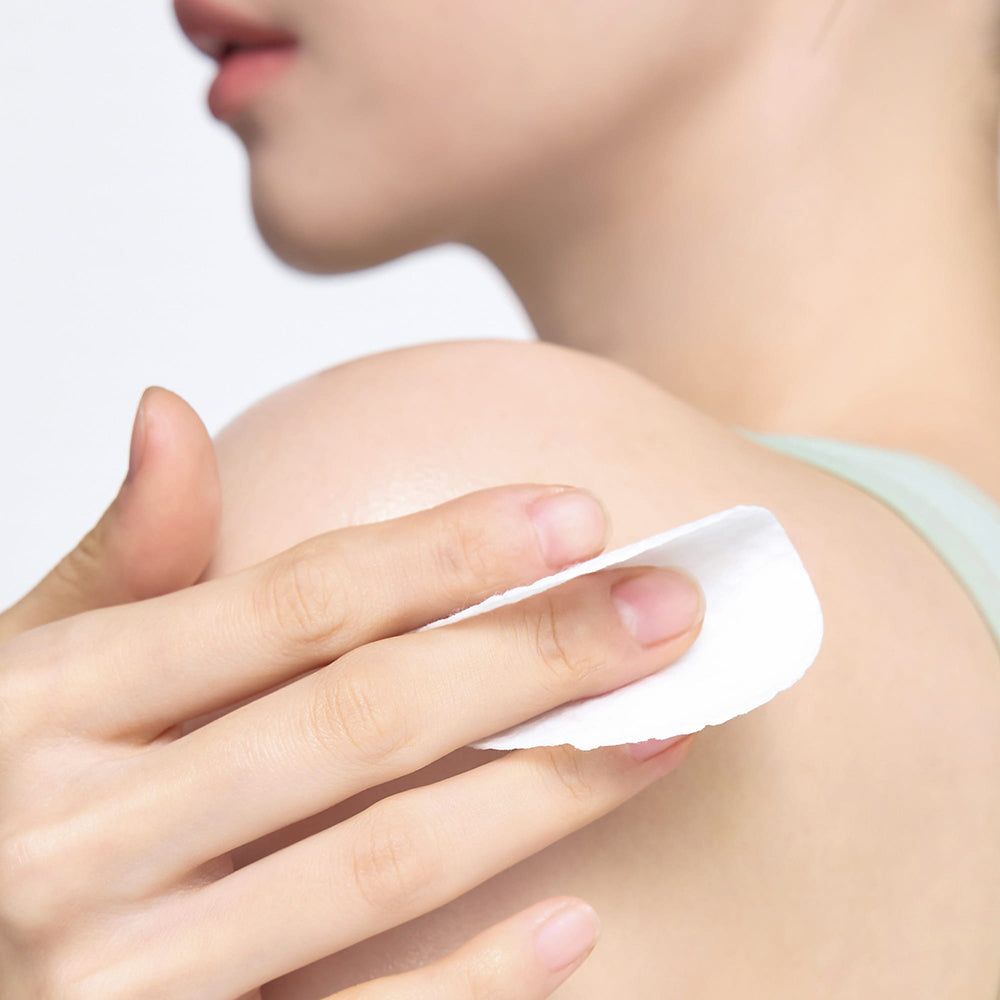Une main utilise un tampon éclaircissant pour le corps CELIMAX Ji Woo Gae sur l'épaule.