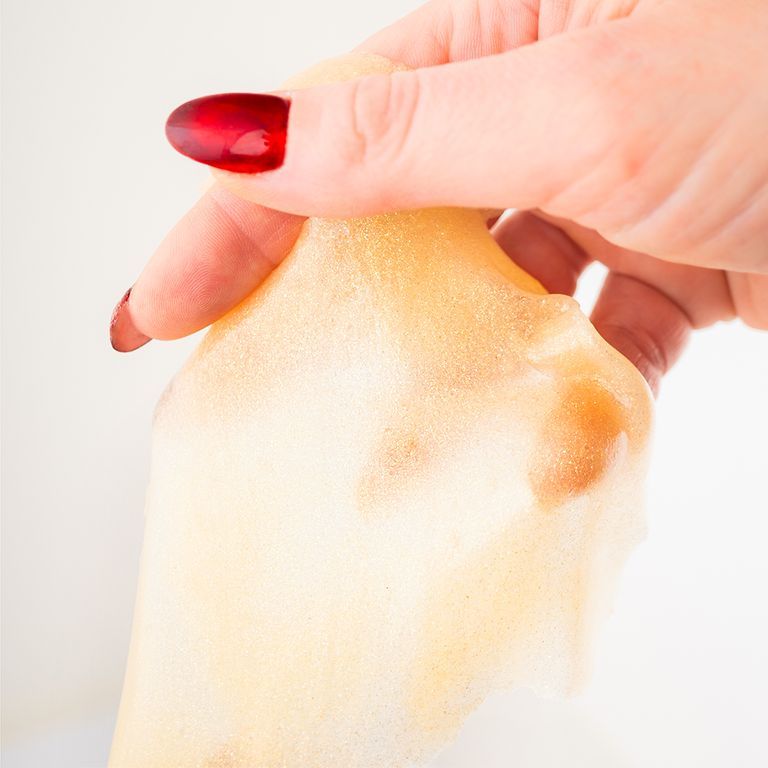 Main tenant un masque facial. Jaune. Ongles rouges. Fond blanc.