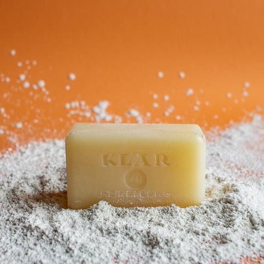 Savon avec l'inscription KLAR sur poudre blanche. Sur fond orange. La poudre entoure le savon.