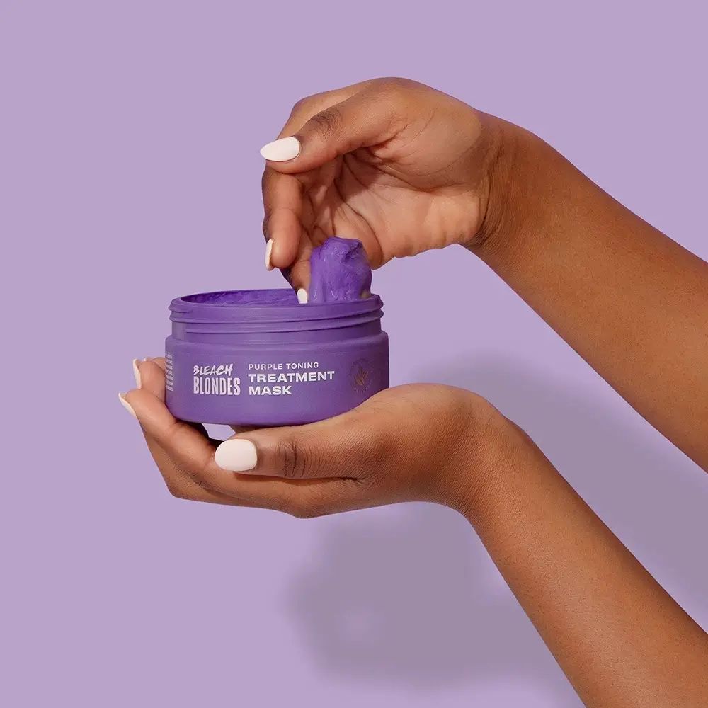 Handen houden een open paarse pot met product vast. Productnaam en logo zichtbaar.