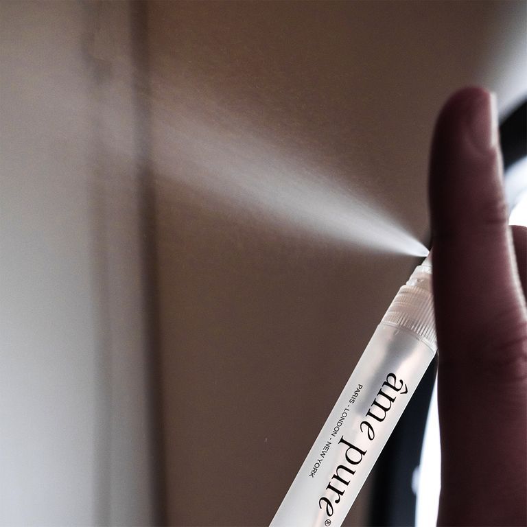 Een hand houdt een klein flesje âme pure handdesinfecterende spray vast, dat een fijne nevel spuit.
