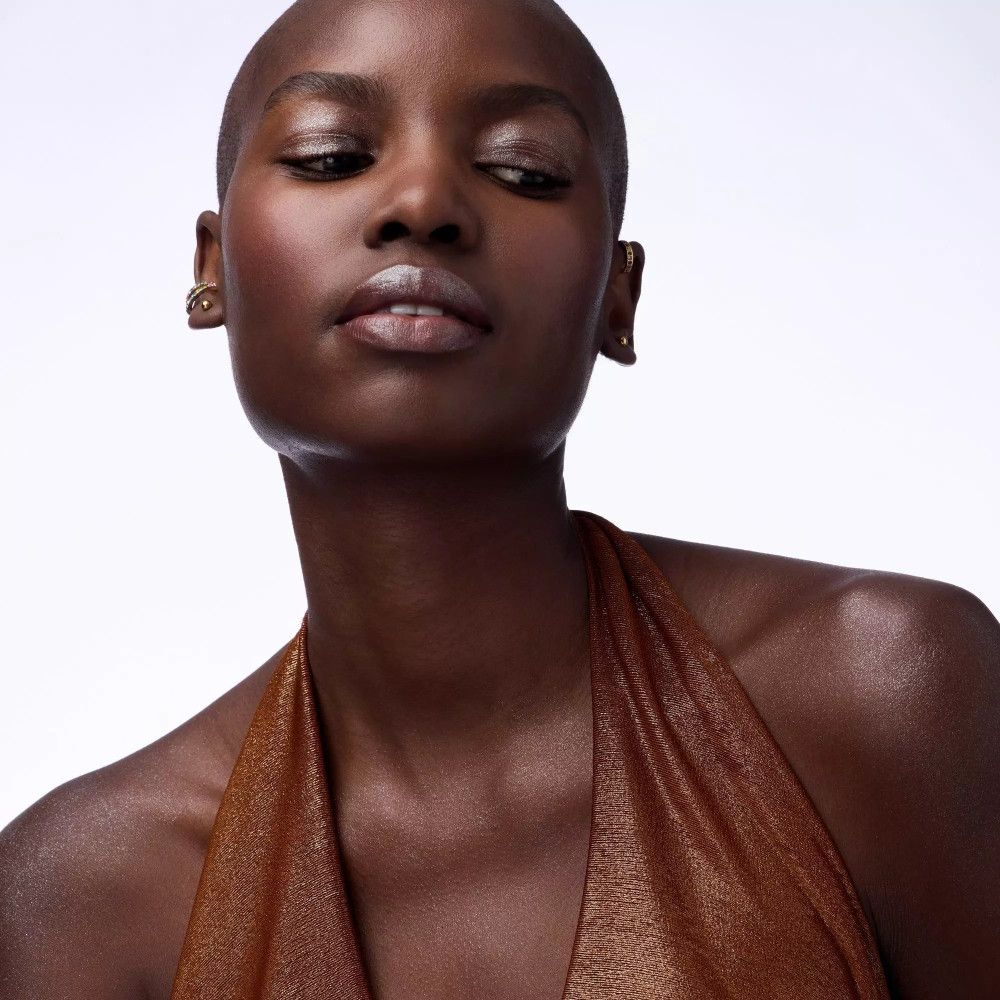 Portrait d'une femme au crâne rasé. Elle porte un haut marron et des boucles d'oreilles. Regard vers le haut.