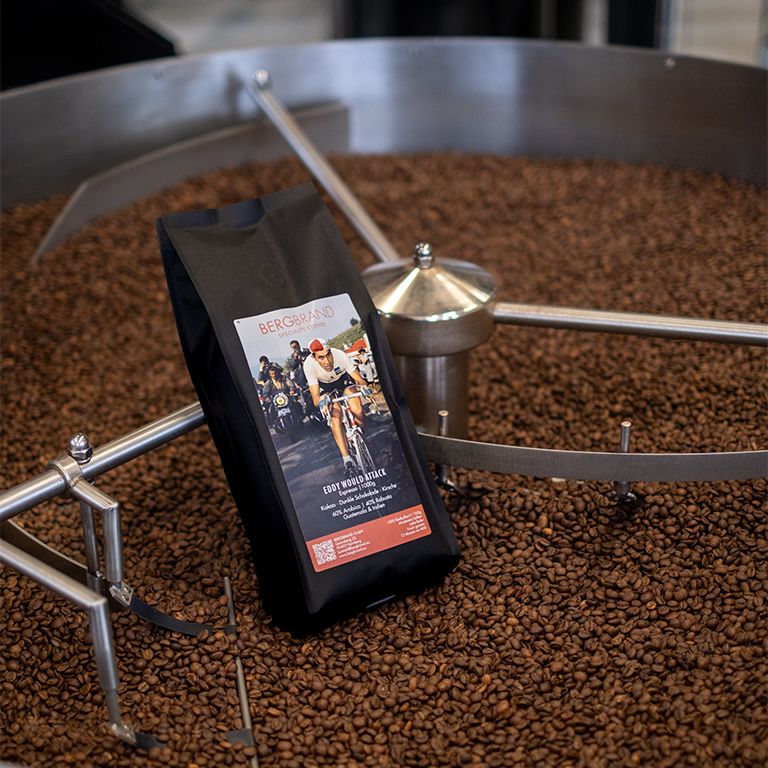 Paquet de café BERGBRAND Eddy Would Attack dans un torréfacteur. Les grains de café entourent le paquet.