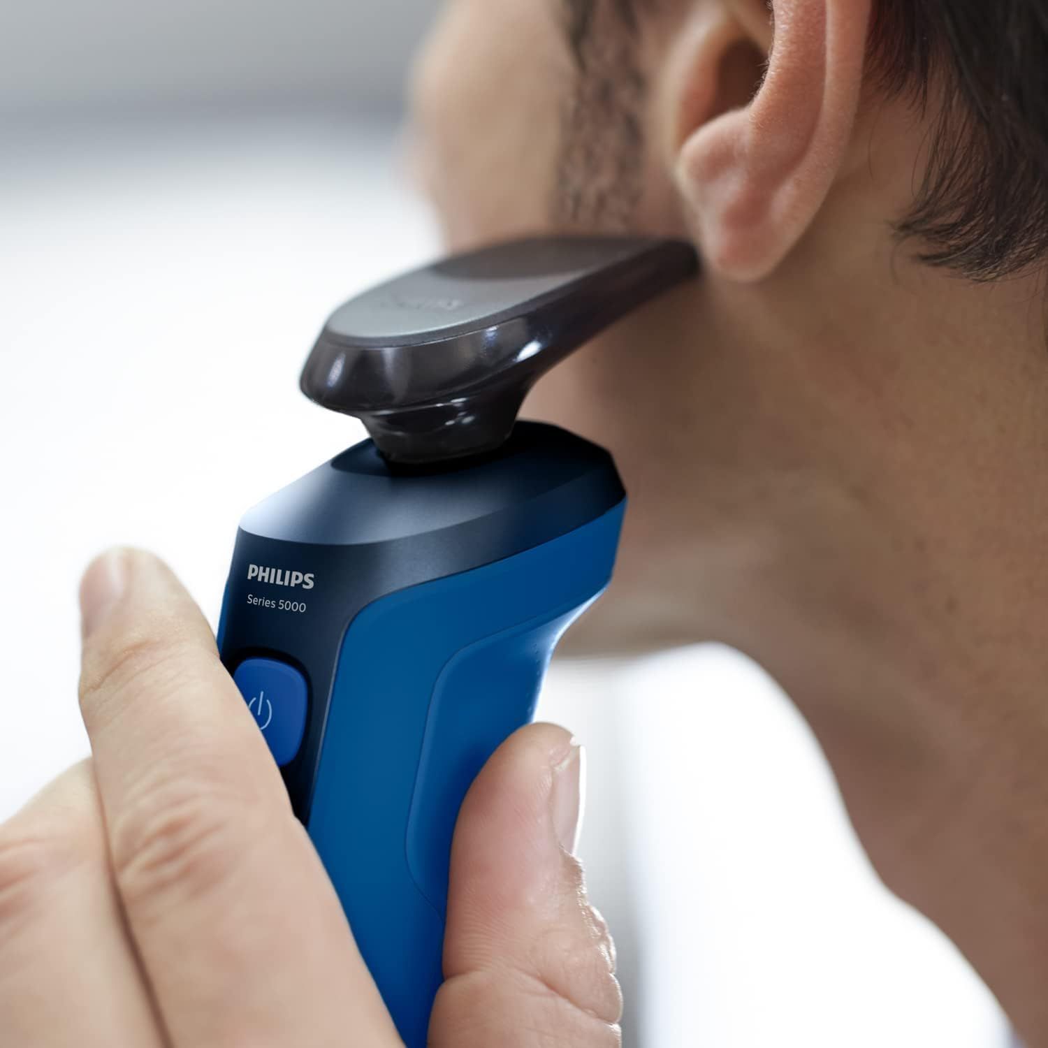 Man scheert zich met blauw elektrisch scheerapparaat. Close-up van gezicht en scheerapparaat.
