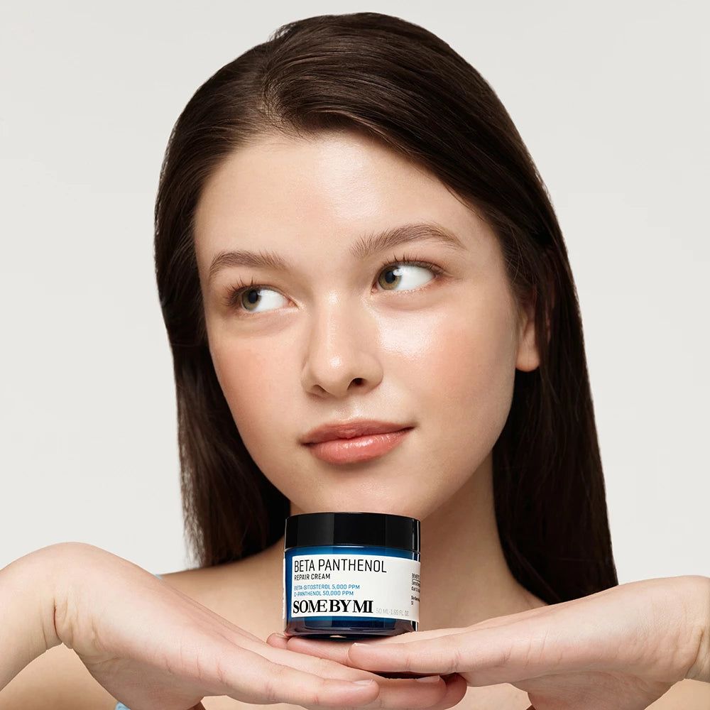 Een vrouw houdt een blauwe crème pot met zwarte deksel vast. Op de pot staat "BETA PANTHENOL" en "SOME BY MI".