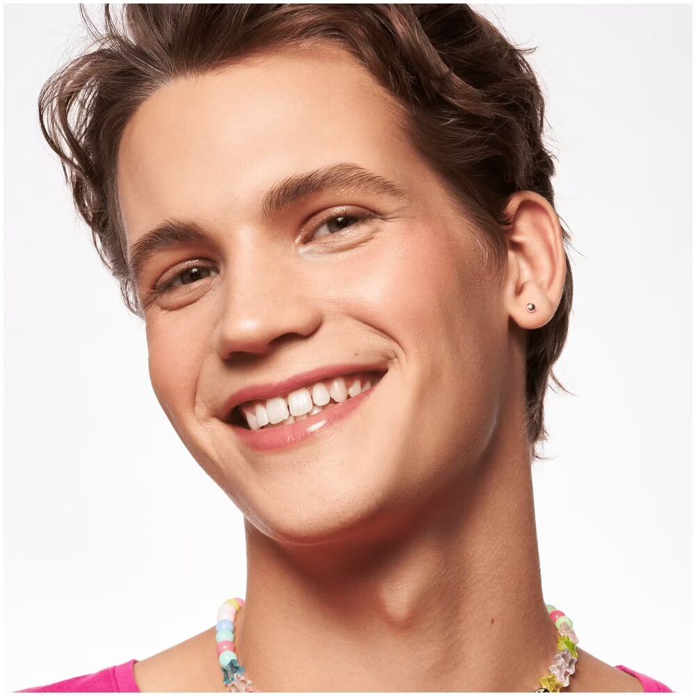 Portret van een man met blush op de wangen. Hij draagt subtiele make-up. Lacht in de camera.