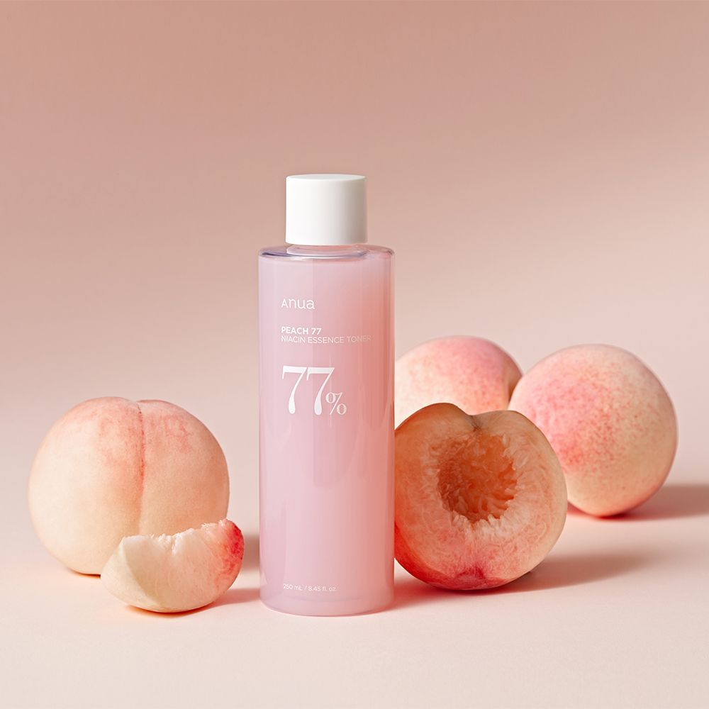 Bouteille de toner essence niacine ANUA Peach 77% entourée de pêches.