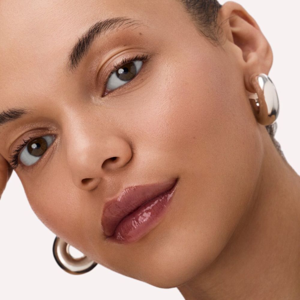 Gros plan d'une femme avec un baume à lèvres brillant sur les lèvres. Boucles d'oreilles dorées.