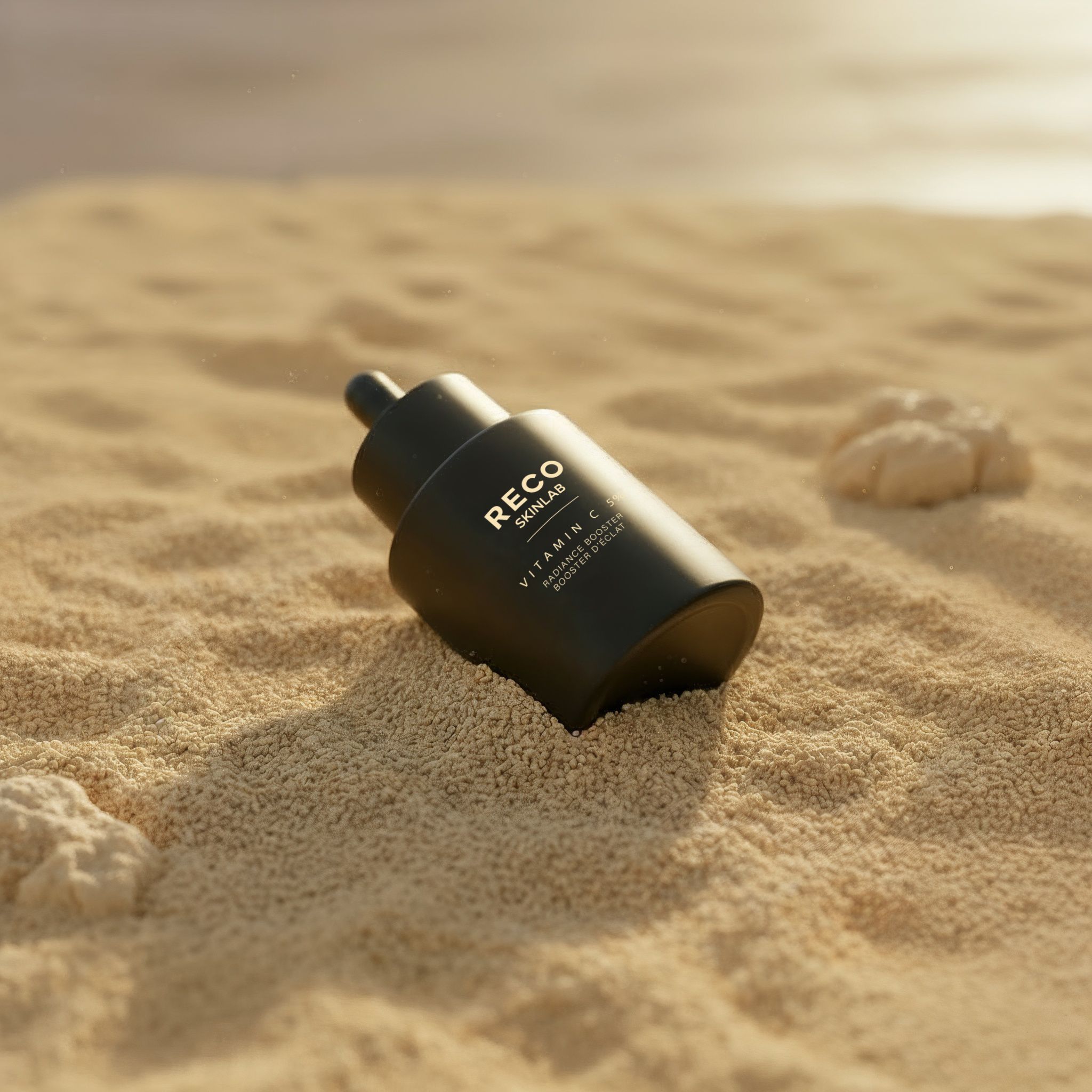 Flacon noir sur sable. Inscription: RECO SKINLAB, Vitamin C. Pipette vers le haut.