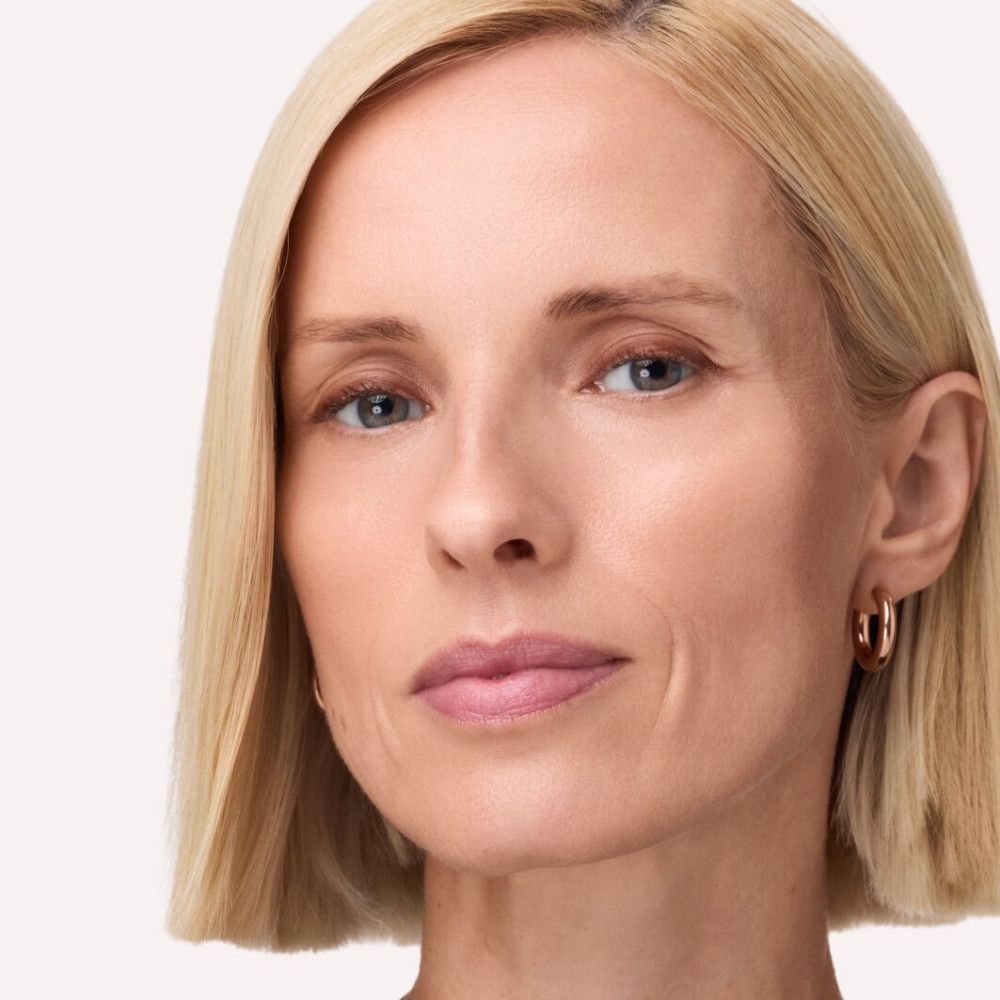 Portrait d'une femme aux cheveux blonds et aux lèvres roses. Elle porte des boucles d'oreilles.