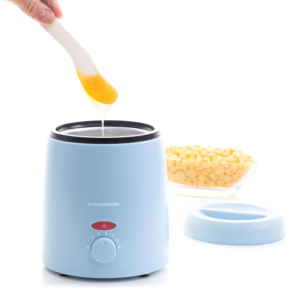 Chauffe-cire bleu avec couvercle et spatule. Application de cire. À côté, perles de cire dans un bol.