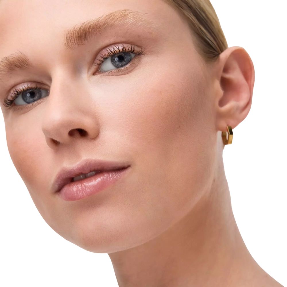 Close-up van een gezicht met blauwe ogen en gouden oorbellen. Witte achtergrond.