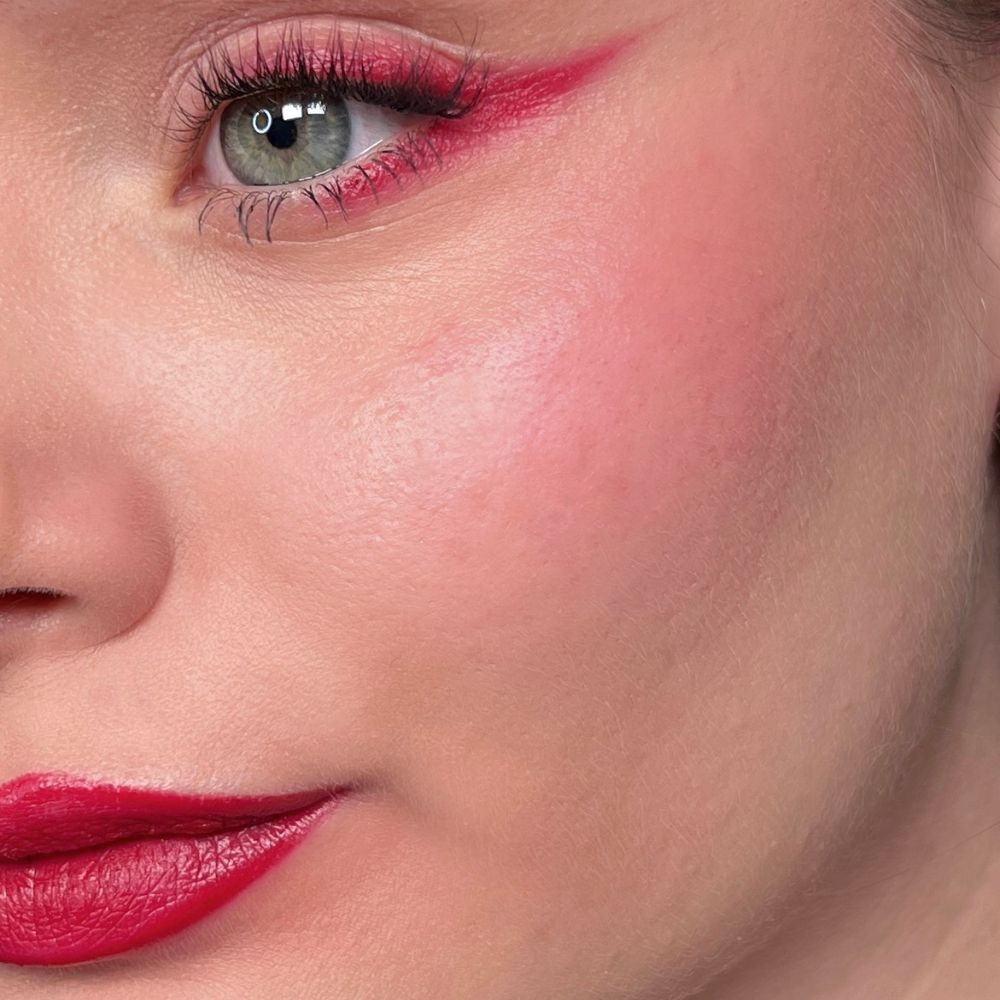 Gros plan d'un visage avec rouge à lèvres, fard à joues et eye-liner rouges. Œil vert.
