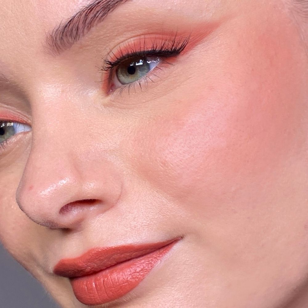 Close-up van een gezicht met opgemaakte ogen, wangen en lippen. Koraalrode lippenstift. Lichte huidskleur.