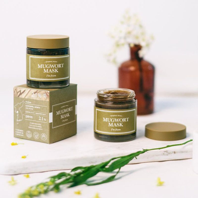 Twee glazen potten met "Mugwort Mask" etiket, een doos en een deksel. Op een oppervlak.