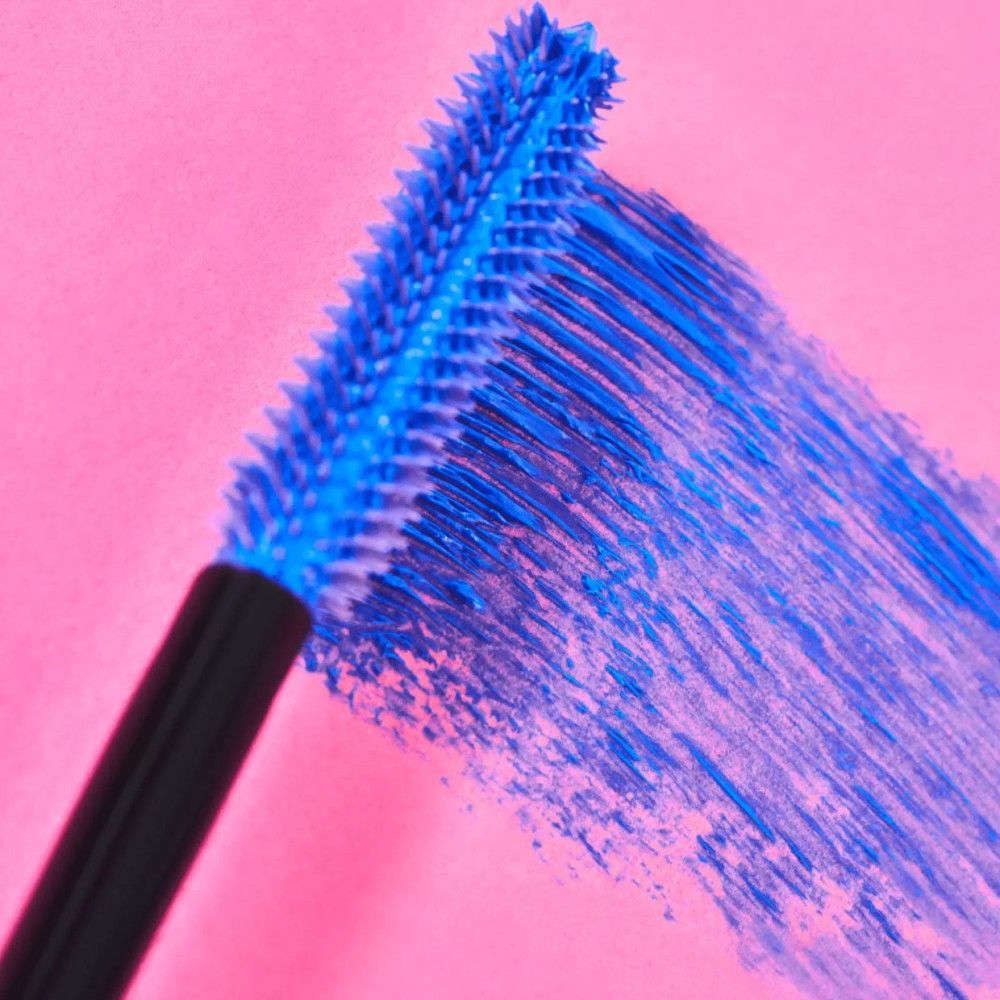 Brosse de mascara bleue avec de la couleur bleue sur fond rose. Soies recouvertes de mascara.