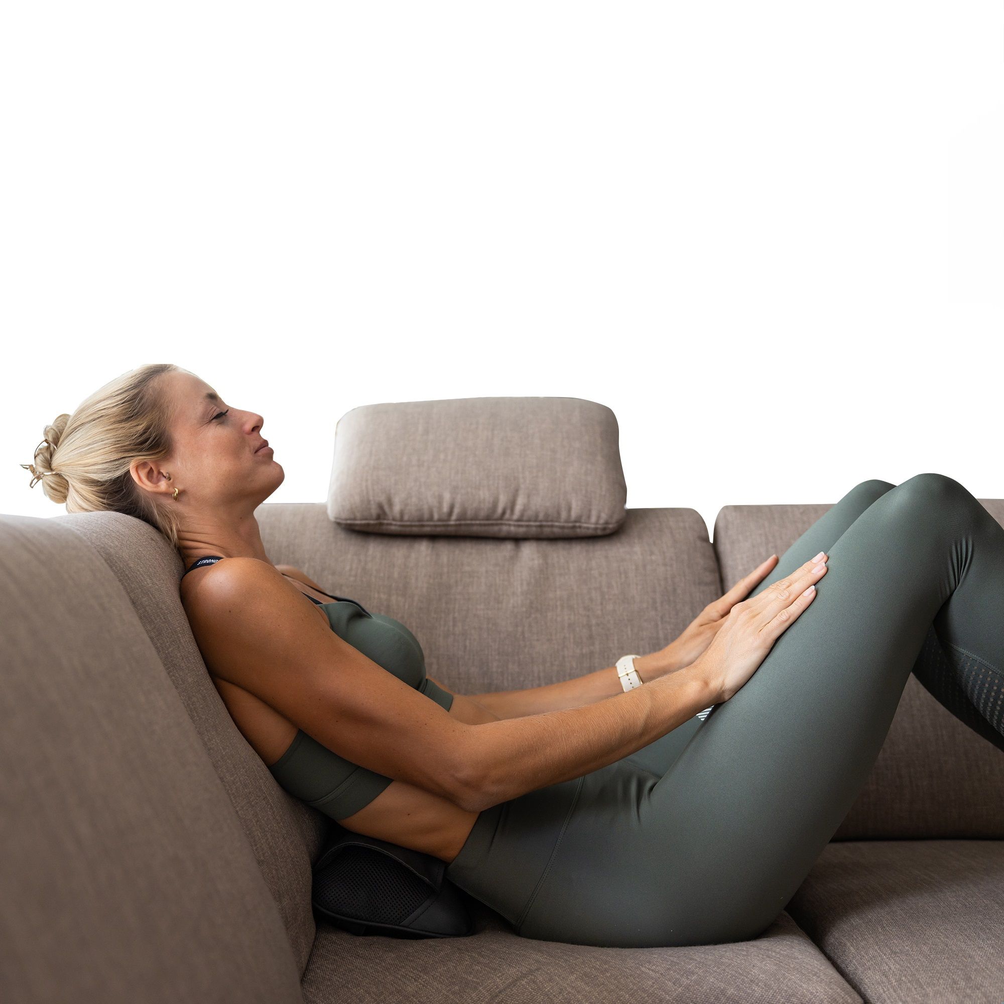 Vrouw ligt op de bank, massagekussen op de onderrug. Zwart kussen. Vrouw in sportkleding.