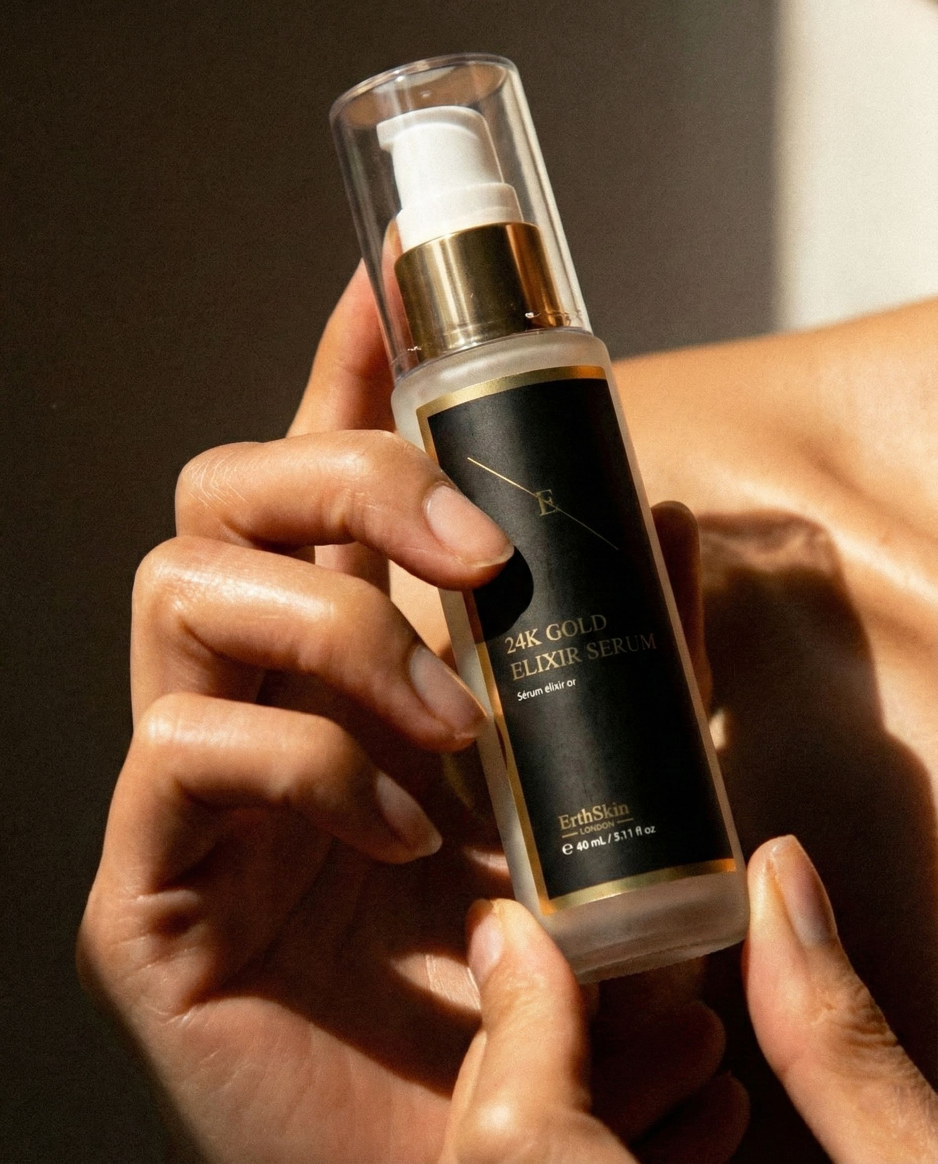 Handen die een fles 24K Gold Elixir Serum vasthouden.