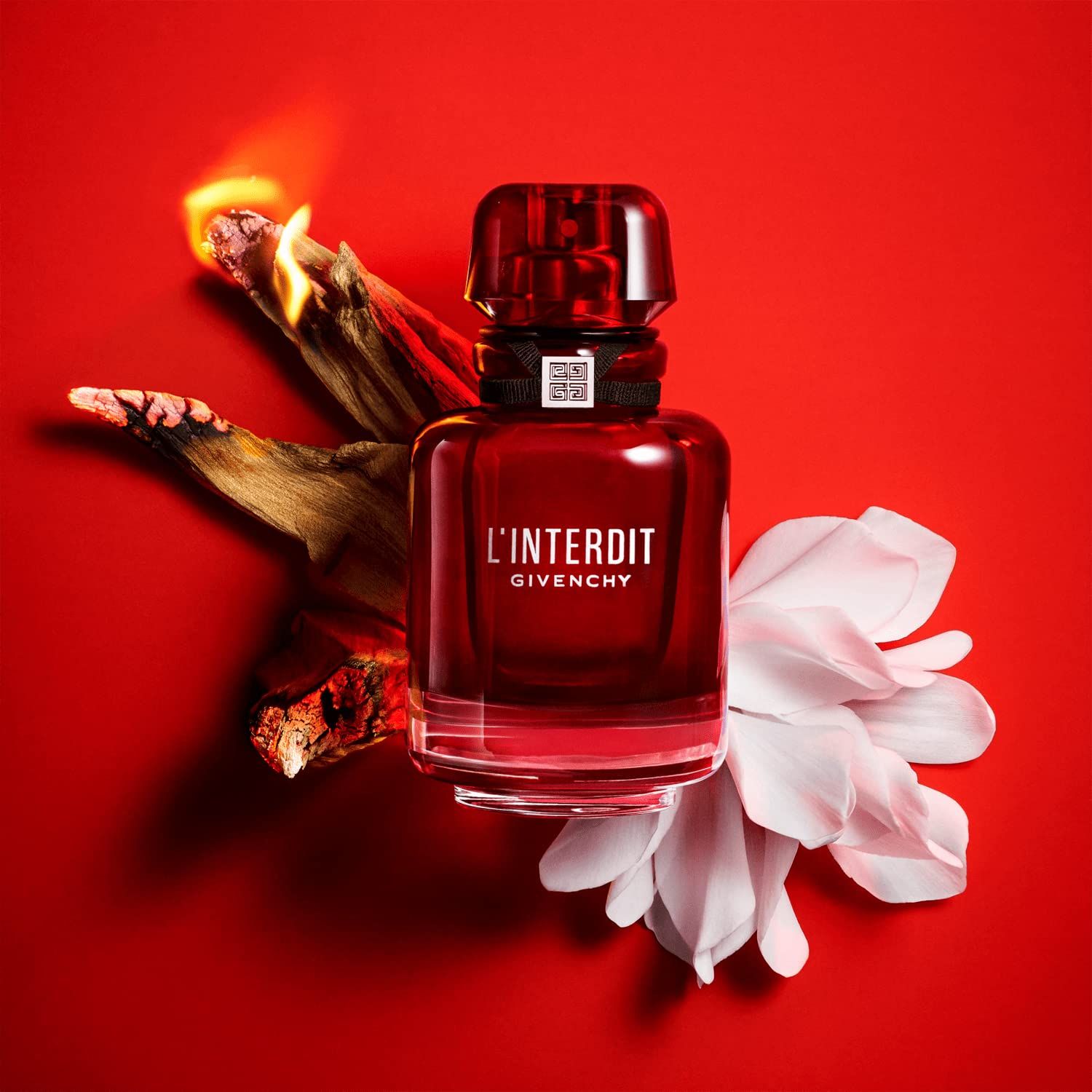 Rode fles van Givenchy L'Interdit Eau de Parfum Rouge. Met hout en bloem op rode achtergrond. Zwart lint met logo.