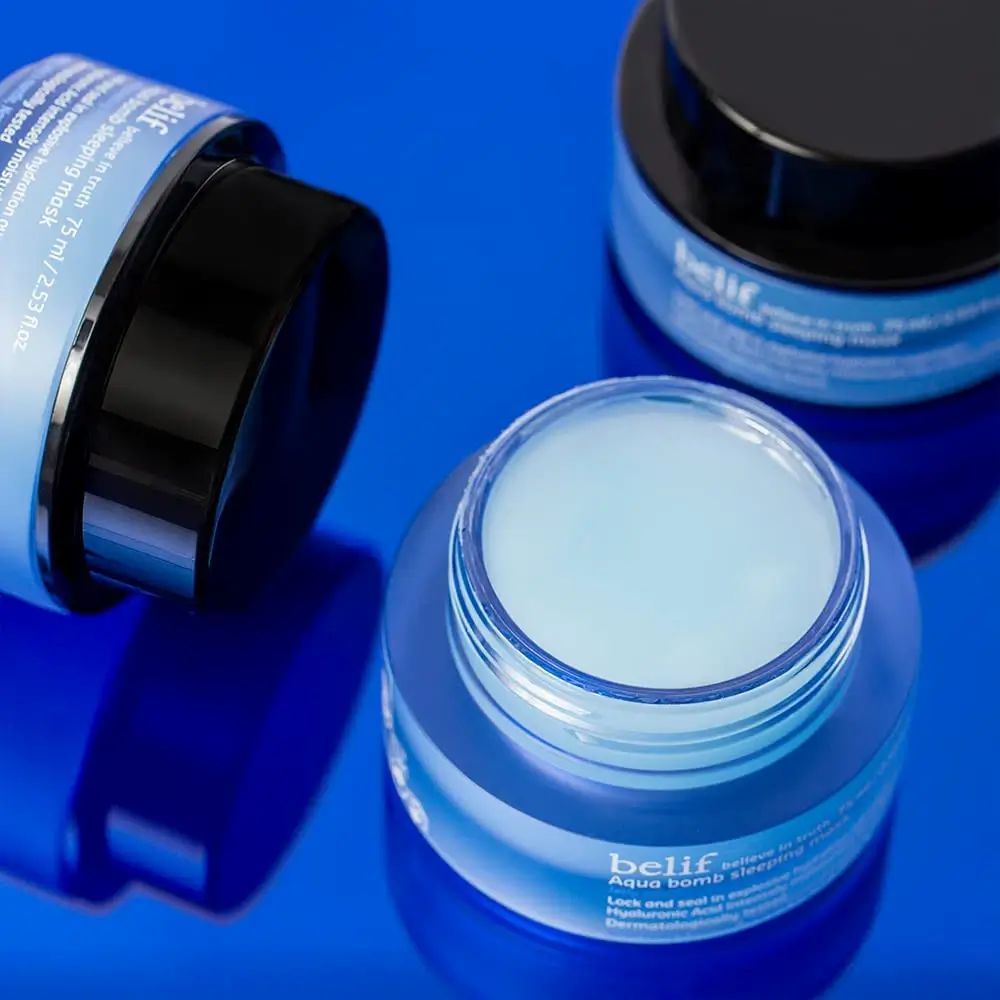 Drie blauwe potten met zwarte deksels. Eén pot geopend, inhoud zichtbaar. Opschrift: belif, Aqua bomb sleeping mask.