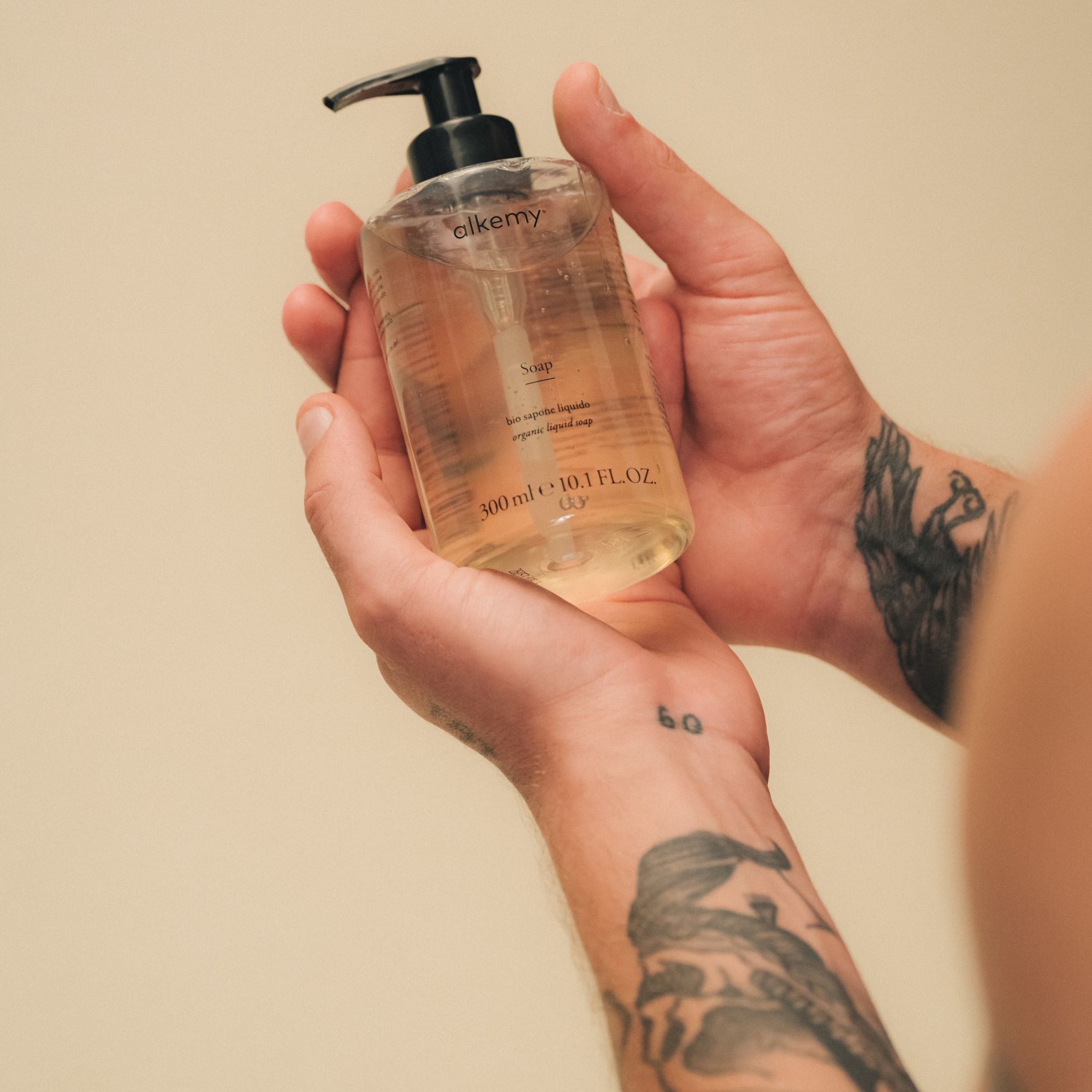 Handen met tatoeages houden fles heldere vloeibare zeep vast.