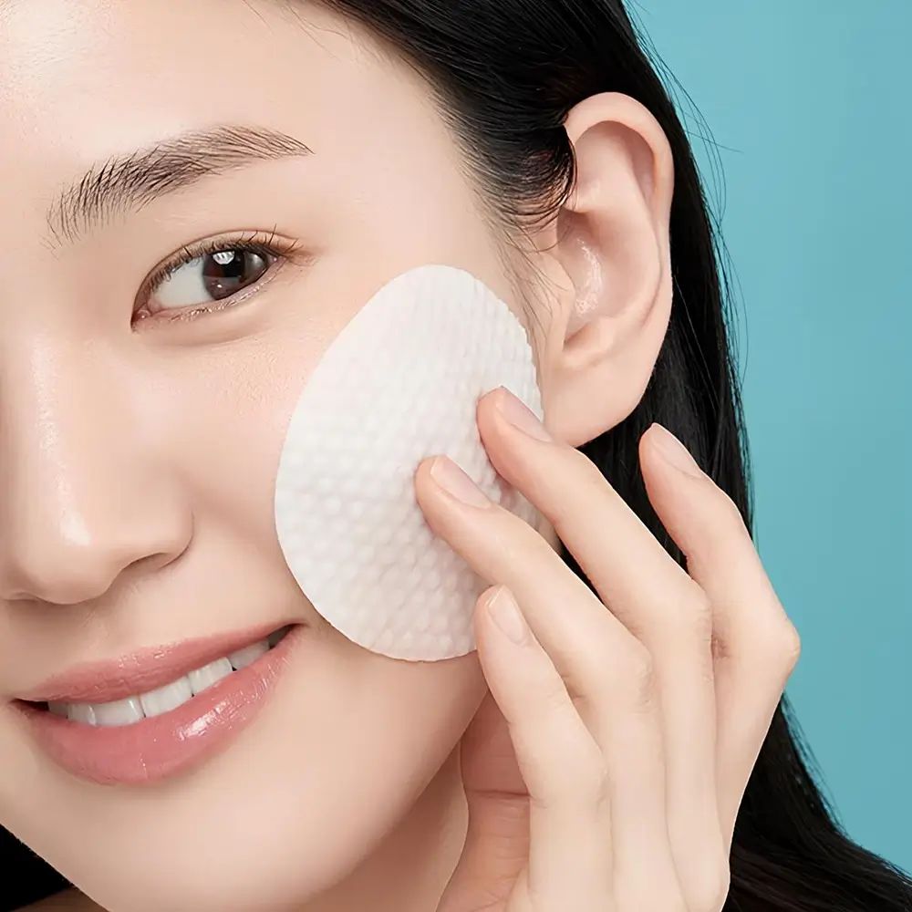 Vrouw met een pad op de wang. De pad is wit en heeft een gestructureerd oppervlak. Blauwe achtergrond.