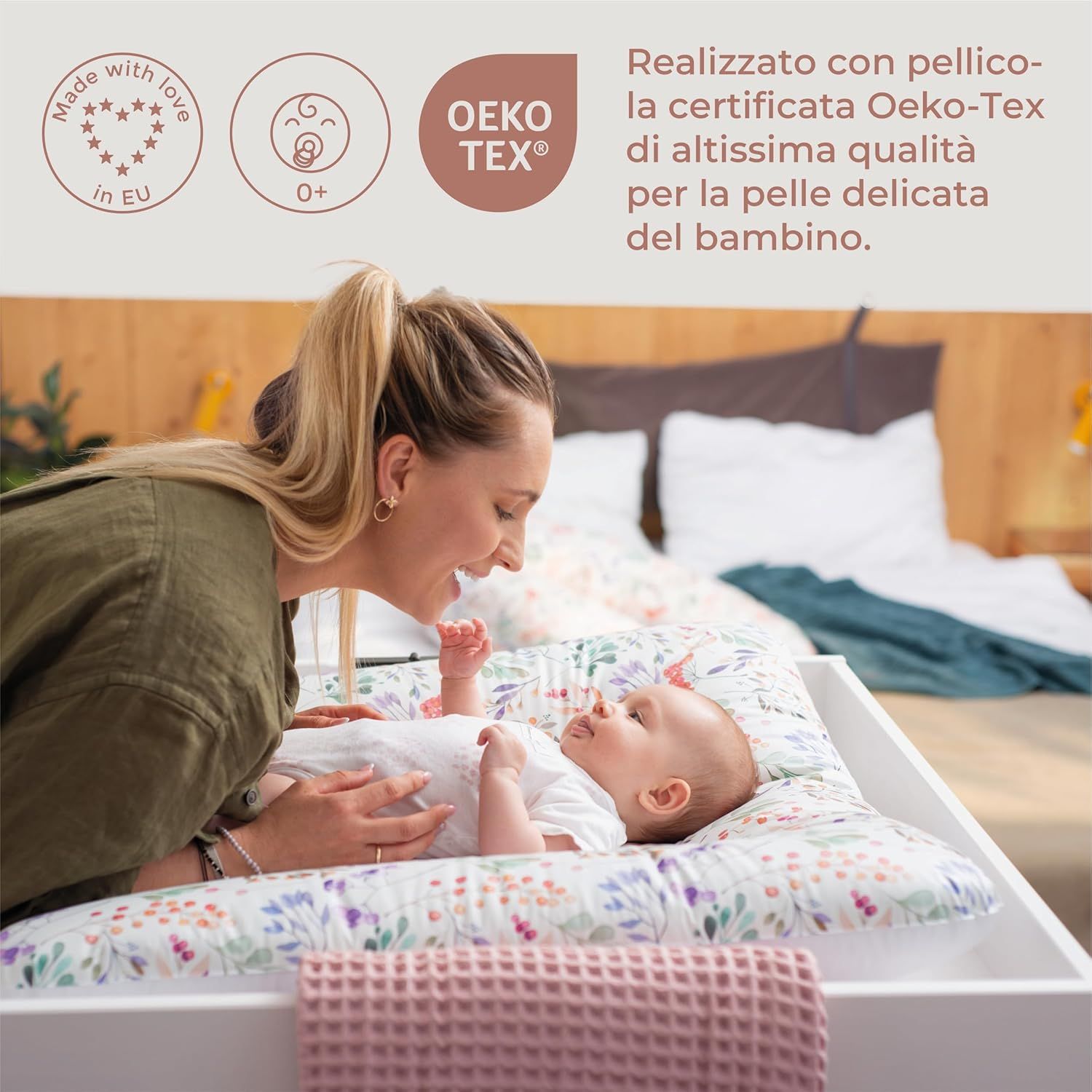 Baby op aankleedkussen met bloemenpatroon. Vrouw kijkt naar de baby. Oeko-Tex-certificering en EU-keurmerk.