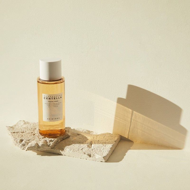 Een fles op een steen. Productlabel met tekst: MADAGASCAR CENTELLA TONING TONER. Witte dop.