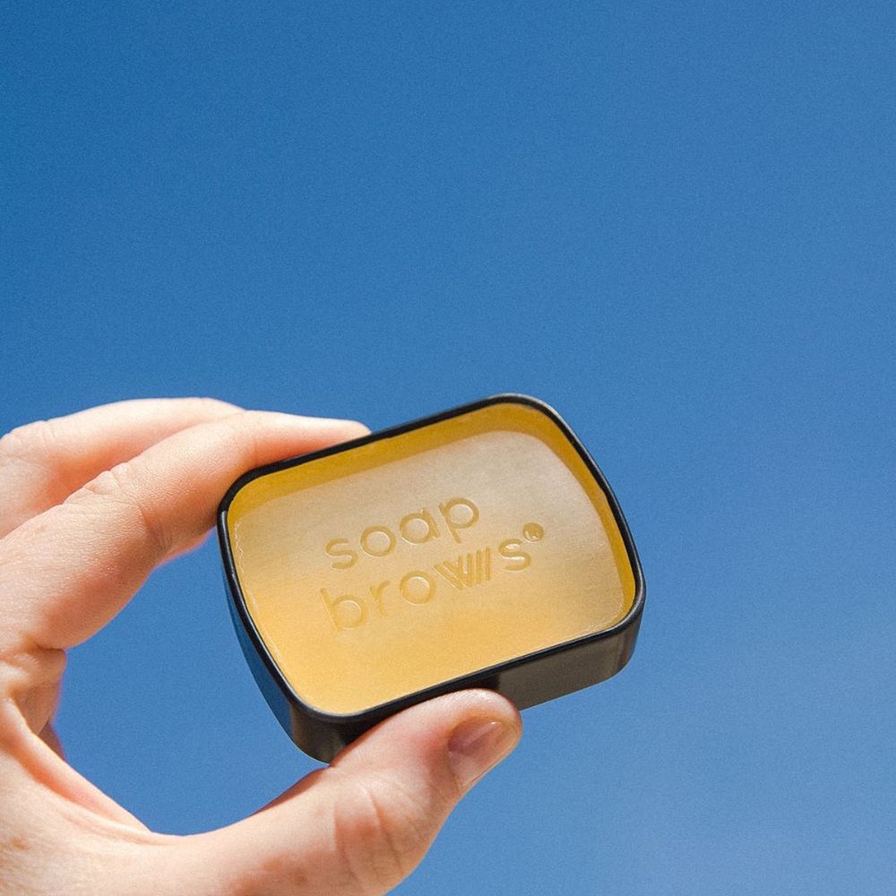 Main tenant un petit boîtier Soap Brows. Le nom du produit est imprimé sur la surface.