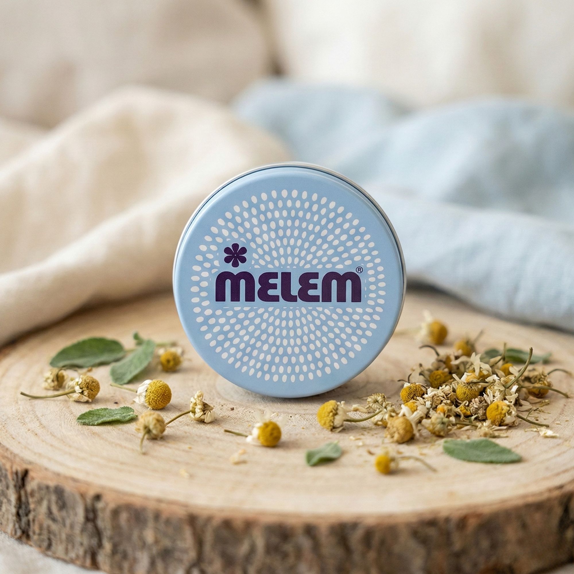 Lichtblauwe, ronde pot met "MELEM" logo op een houten plank, omringd door gedroogde bloemen en bladeren.