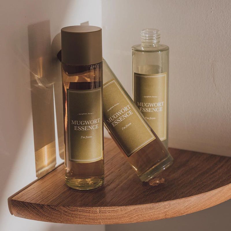 Drie flessen op een houten plank. Opschrift: Mugwort Essence. Gouden doppen en etiketten.