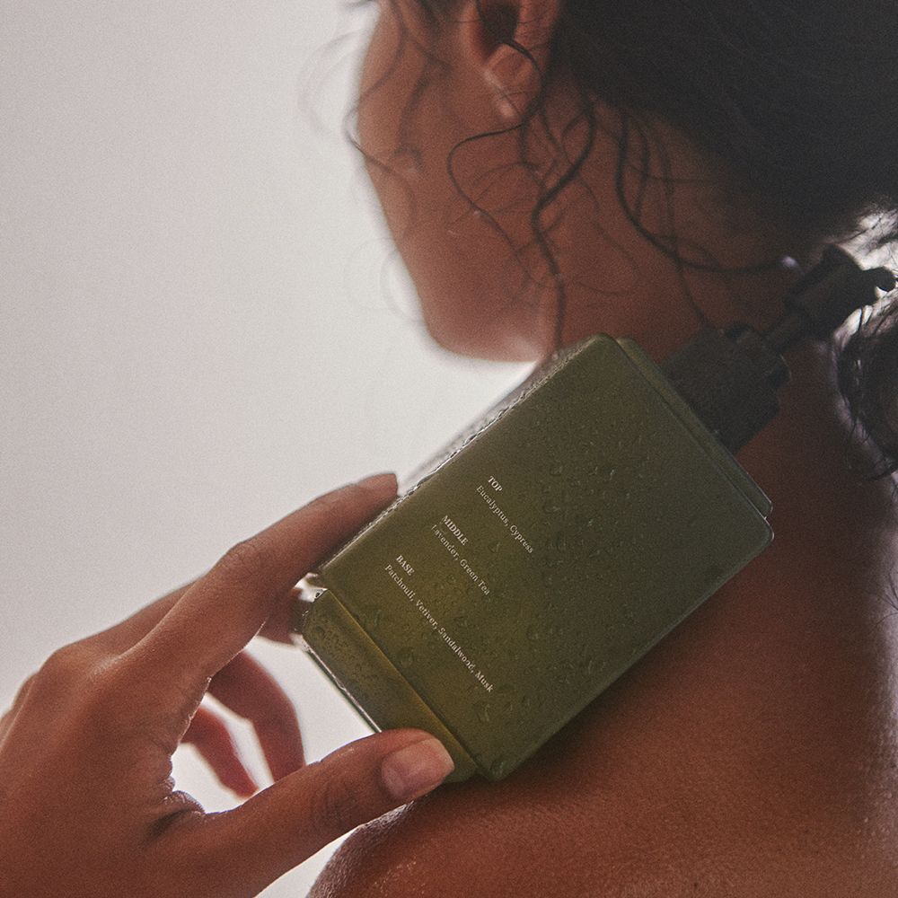 Groene fles met zwarte pomp, gedeeltelijk bedekt. Opschrift: Hand & Body Wash. Merk: VILLAGE 11 FACTORY.