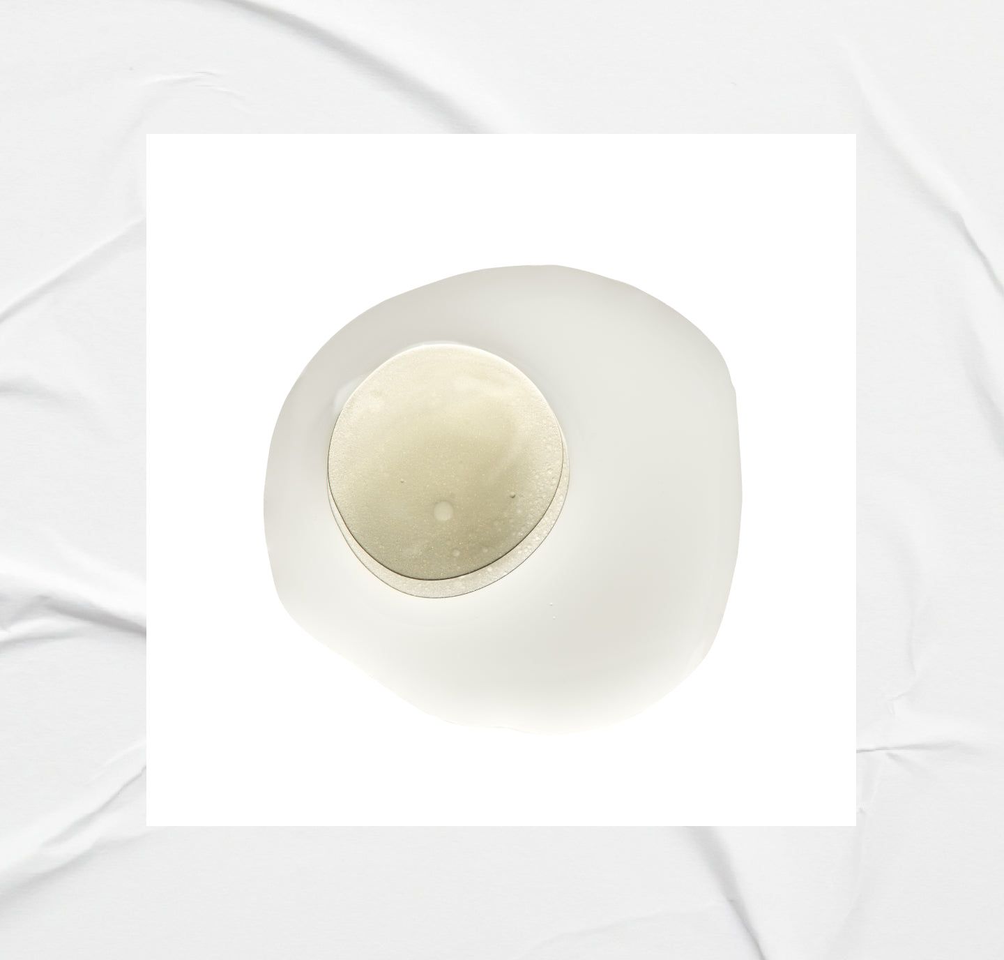 Fond blanc avec une goutte de liquide et un objet rond au centre.