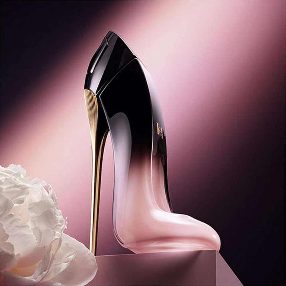 Flacon de parfum en forme de chaussure. Dégradé noir-rose, talon doré. Placé sur un piédestal, fond rose.