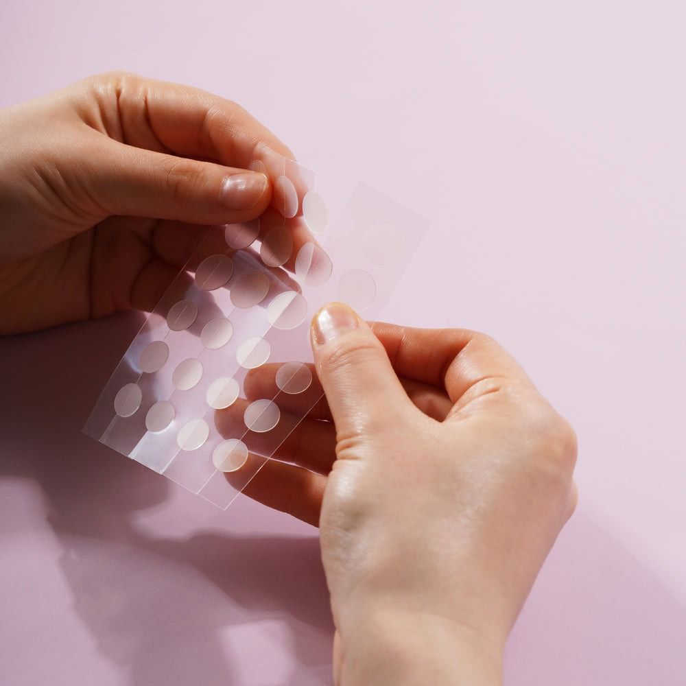 Handen die een transparante folie met ronde pleisters vasthouden. Pleisters zijn zichtbaar.