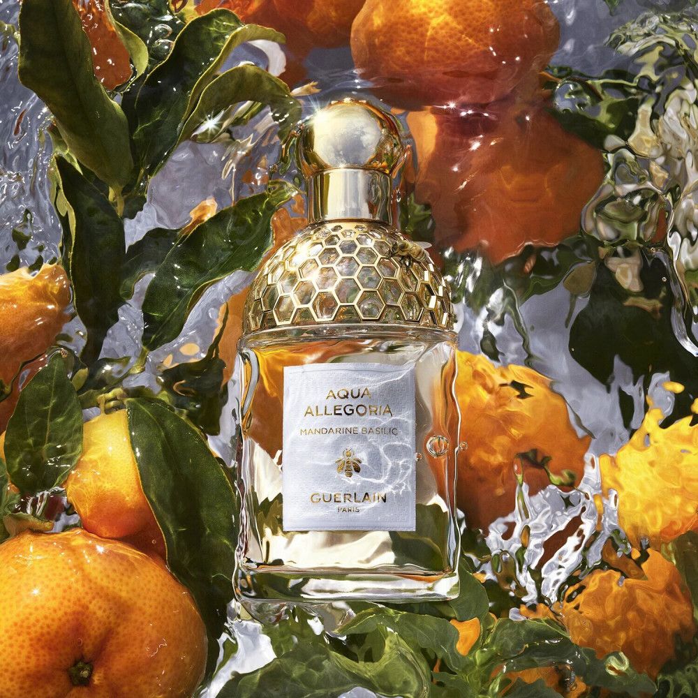 Parfumfles in water met mandarijnen en bladeren. Opschrift: Aqua Allegoria Mandarine Basilic, Guerlain.