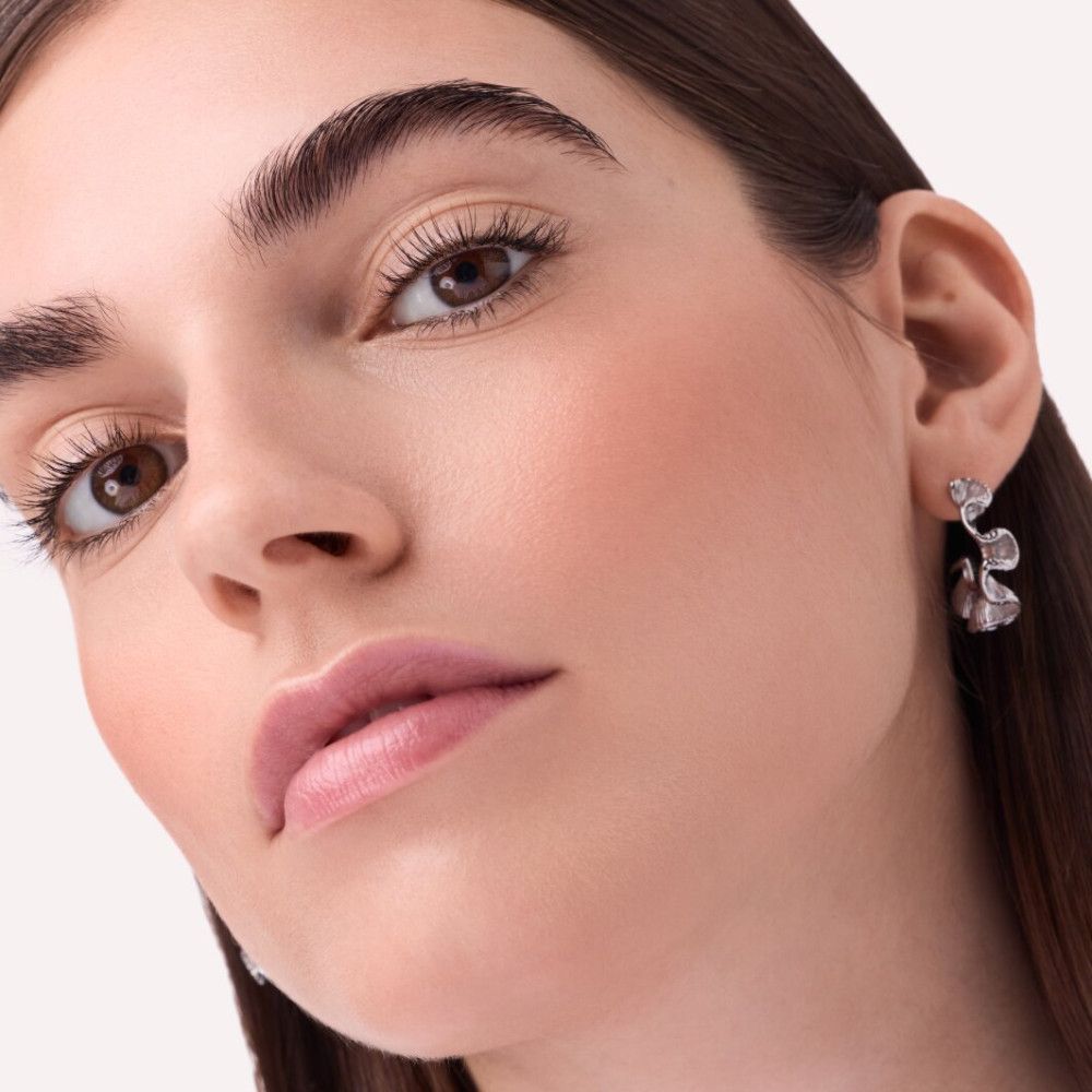 Gros plan d'une femme avec du blush sur les joues. Elle porte des boucles d'oreilles. Lumière naturelle.