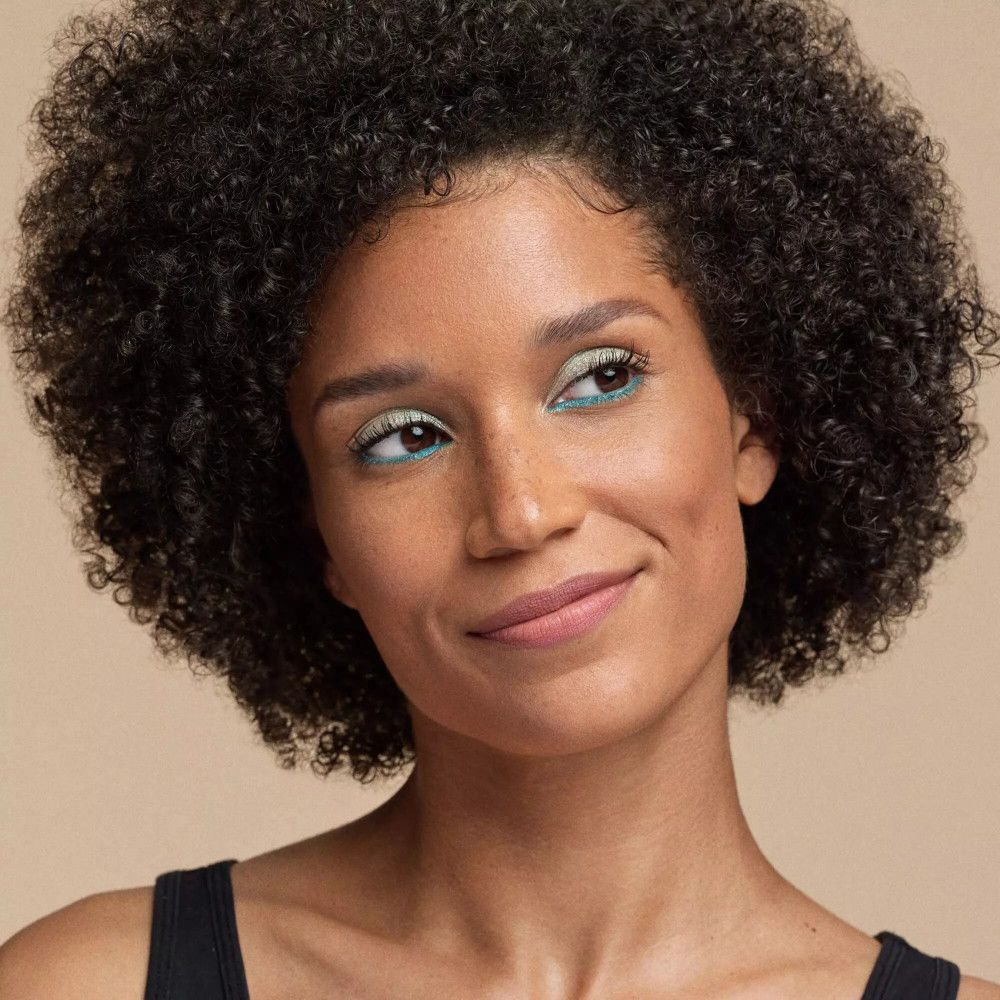 Portrait d'une femme avec rouge à lèvres rose clair, eye-liner bleu et boucles d'oreilles dorées.