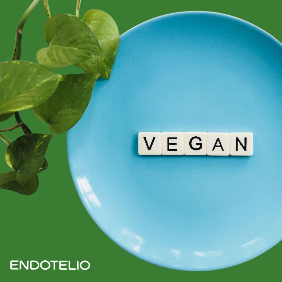 Blauw bord met het woord 'VEGAN' in witte letters. Groene achtergrond. Endotelio-logo linksonder.