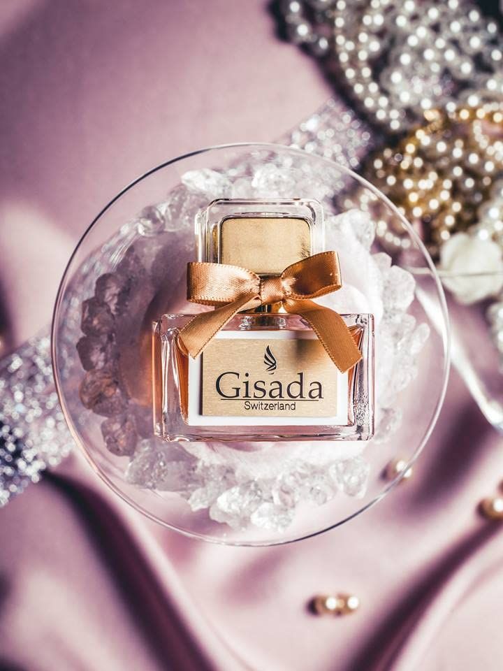 Gisada parfumfles met gouden strik en etiket, op ijsblokjes in een glazen schaal.