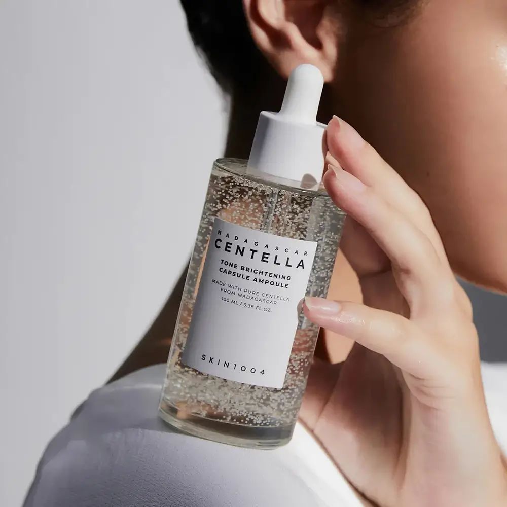 Transparante glazen fles met pipet. Opschrift: CENTELLA, TONE BRIGHTENING CAPSULE AMPOULE. SKIN1004-logo.