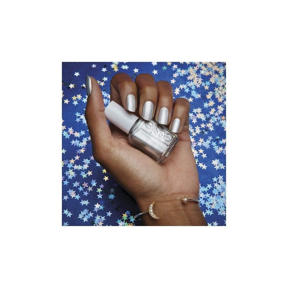 Hand met zilveren nagellak en nagellakfles. Op de fles staat "essie". Armband met maan- en sterbedels.