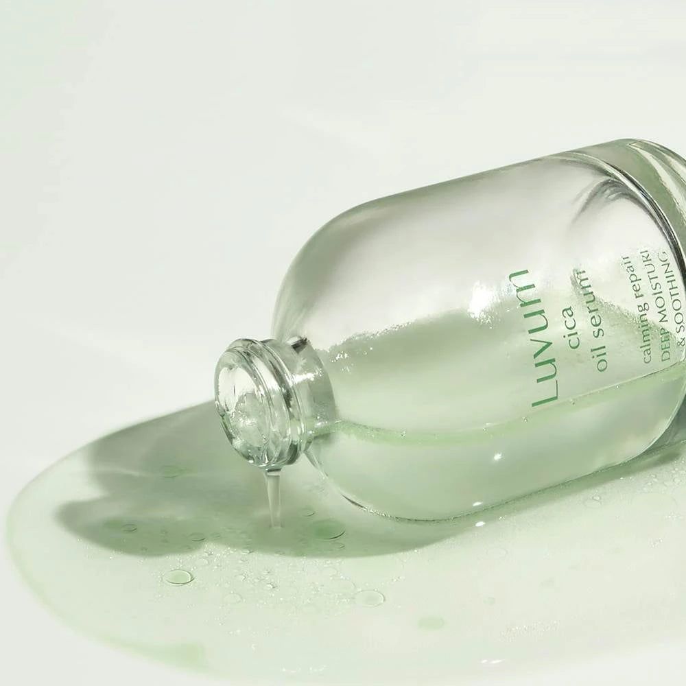 Serumflesje ligt op een oppervlak. Serum vloeit uit de fles. Opschrift: Luvum cica oil serum. Tekst: real calming repair, deep moisture & soothing.