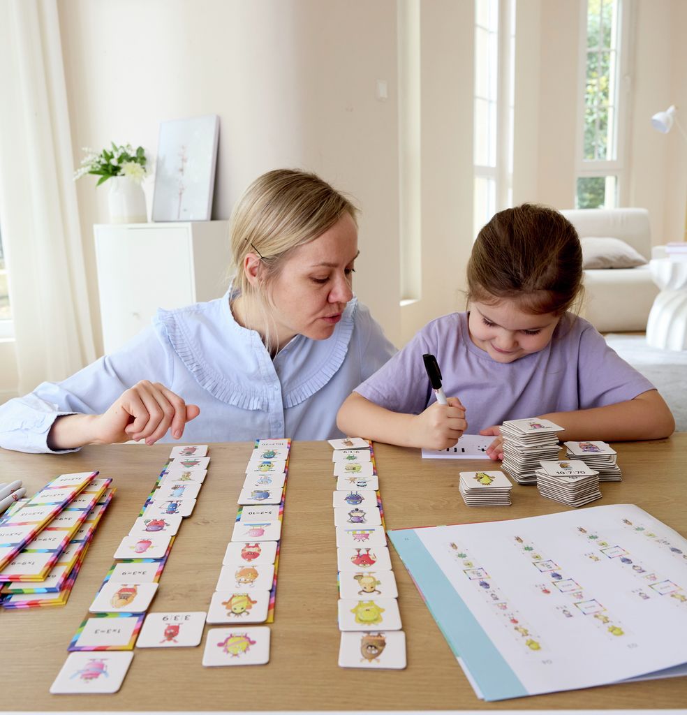 Twee personen spelen Hape Mnemory. Kaarten, stiften en een boek op een tafel. Iemand schrijft op een kaart.
