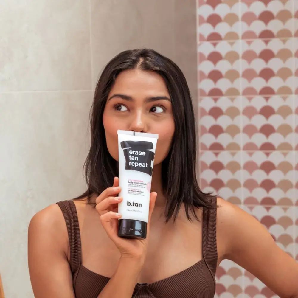 Femme tenant un tube devant son visage. Le tube porte l'inscription "erase tan repeat" et "b.tan".