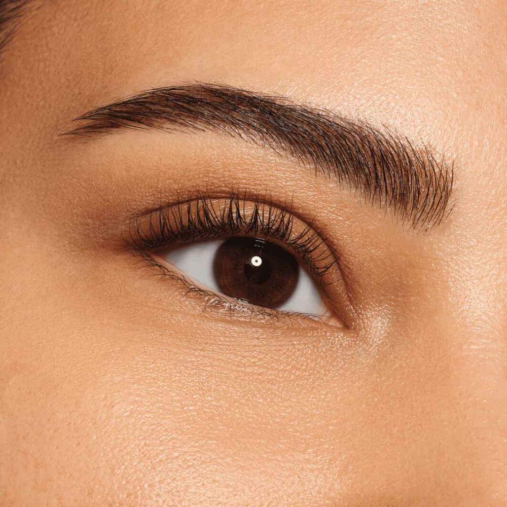 Gros plan sur un œil avec des sourcils façonnés. L'œil est marron et les cils sont maquillés.