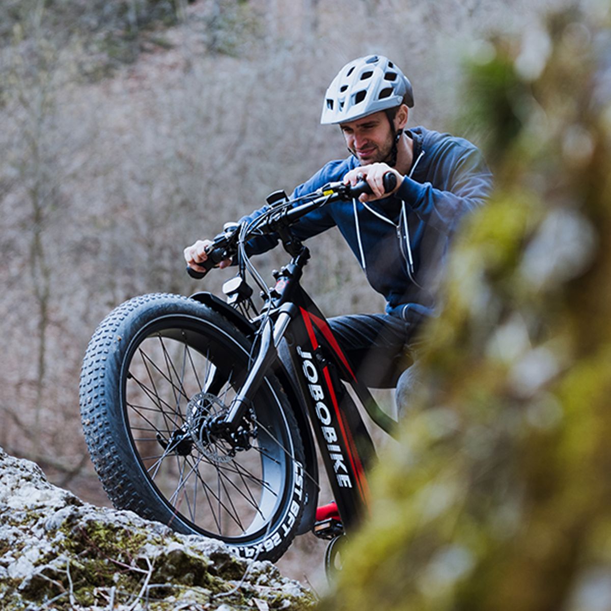 Personne sur un vélo électrique JOBOBIKE Robin. Roule sur un chemin rocheux. Casque et nature en arrière-plan.