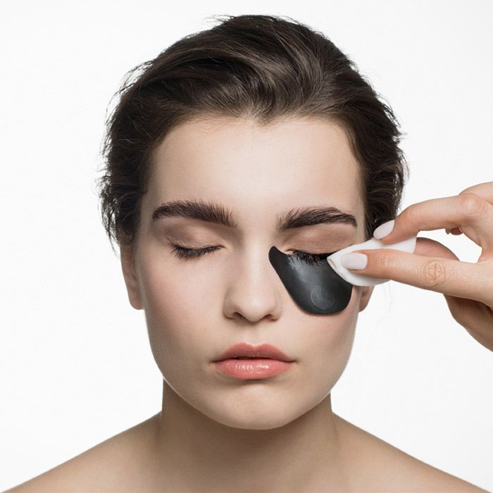 Gezicht van een vrouw met oogpads. Een hand verwijdert een oogpad met een watje.